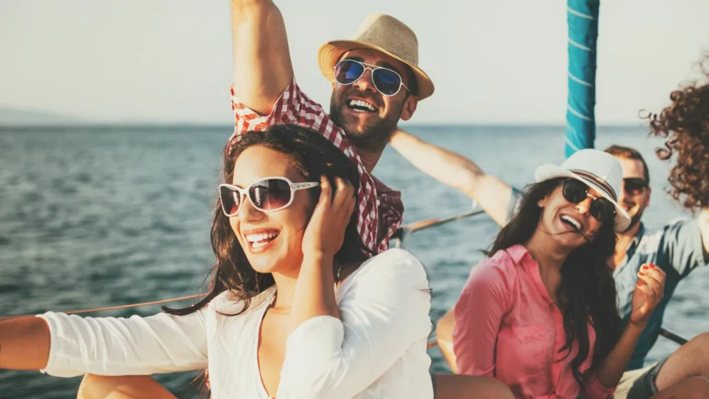 Jóvenes adultos sonriendo y disfrutando en un barco sus vacaciones gestionadas por un agente de viaje.
