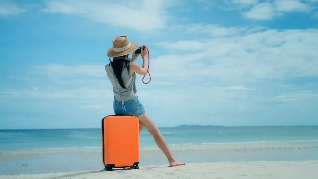 Mujer en la playa, sentada en su maletín trata de fotografíar el momento de sus vacaciones.