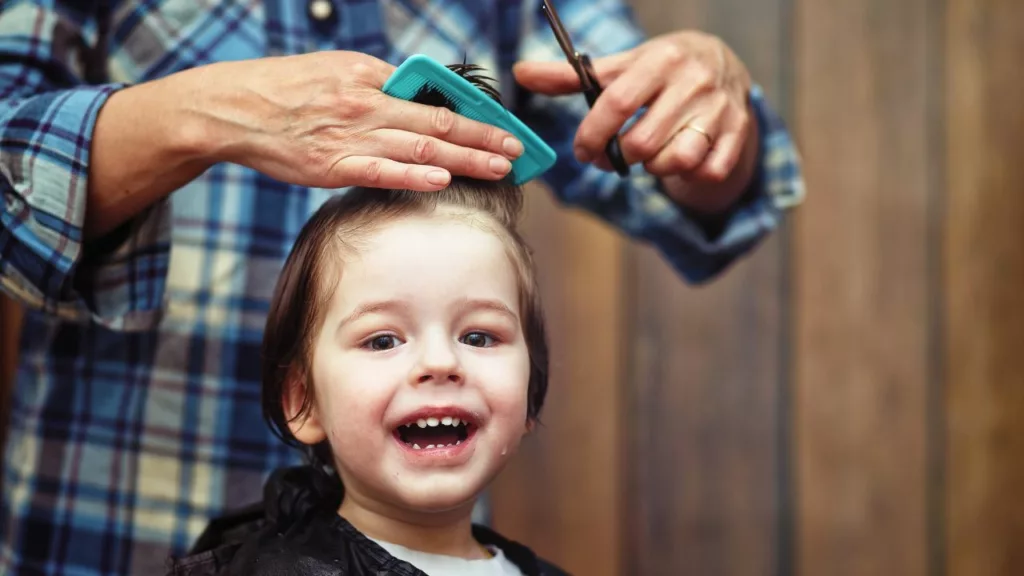 Barbero recortando el pelo de un niño que sonrie.