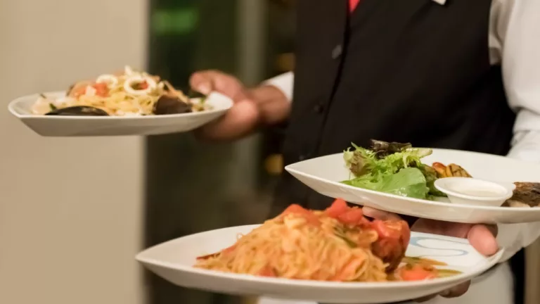 Camarero sosteniendo 3 platos para servir la comida a sus clientes