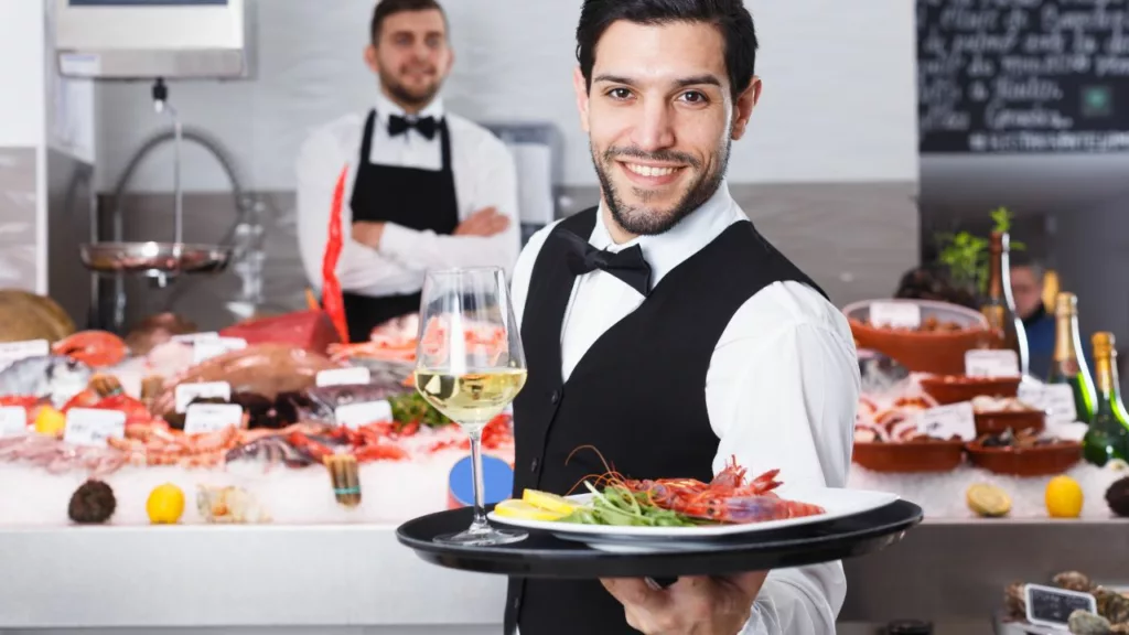 Camarero sosteniendo un plato de mariscos y una bebida.