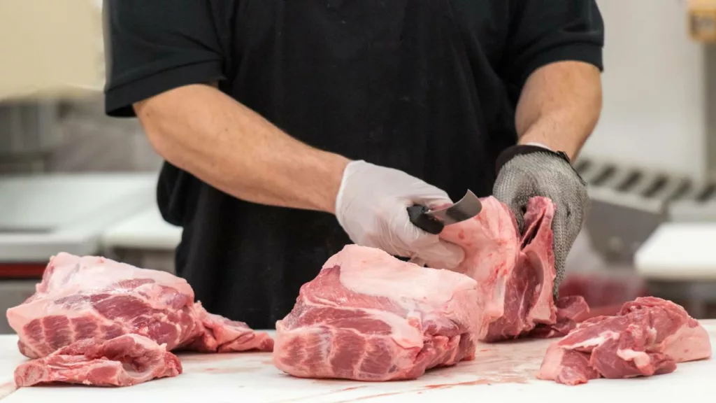 Carnicero profesional cortando partes de carne para vender.