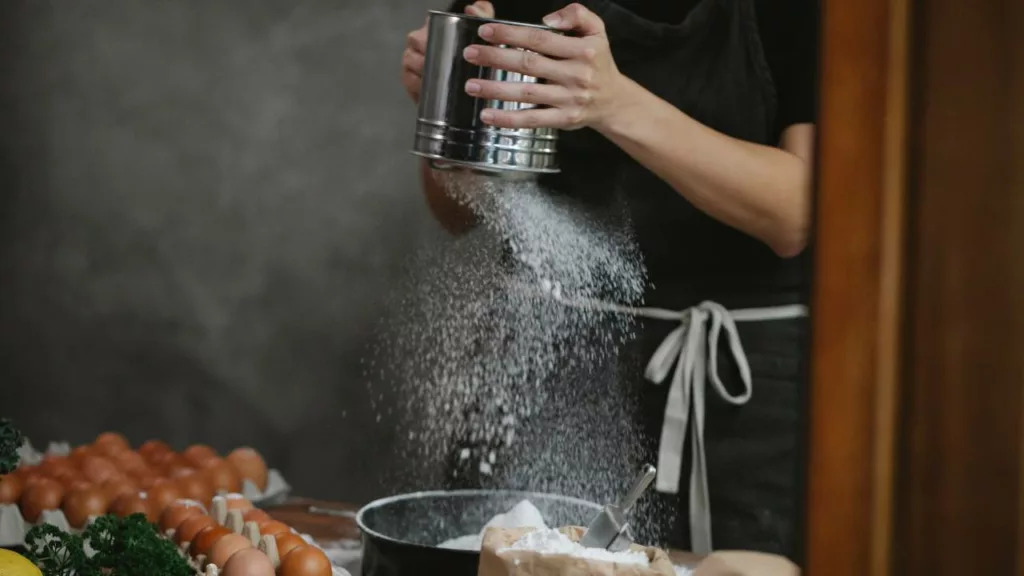 Cocinero echa polvo de harina como ingrediente para el alimento que cocina.