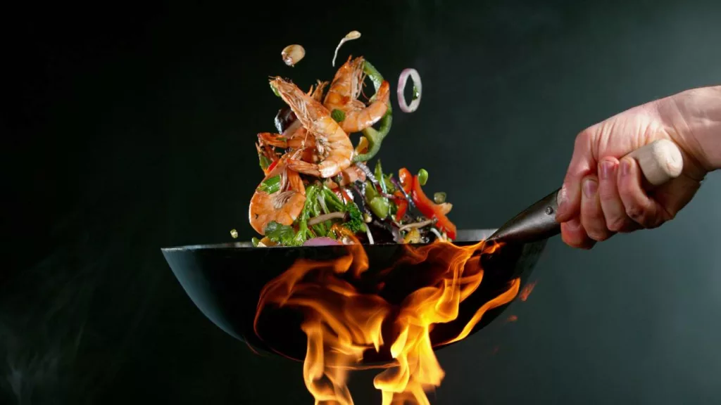 Chef cocinando comida de mariscos en un sartén a fuego alto.