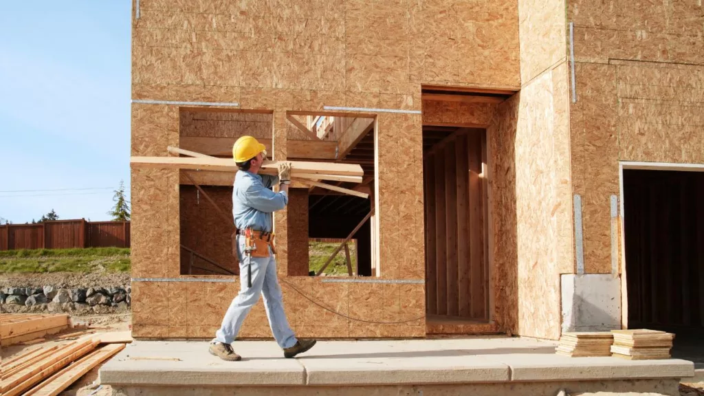Albañil llevando madera en la construcción de una casa.