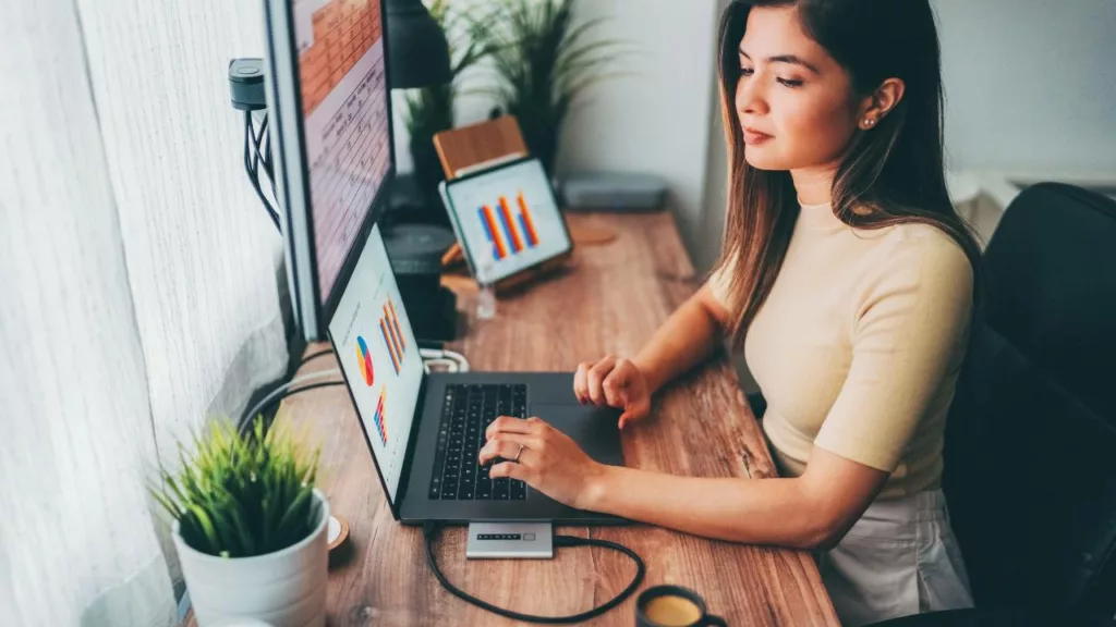 Mujer trabajando como auxiliar administrativa, con una laptop y viendo gráficos e informes.