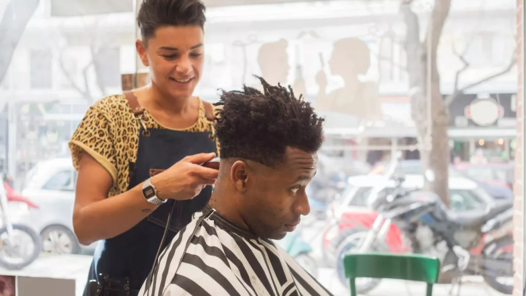 Mujer trabajando en una barbería y recortando el pelo de un hombre.