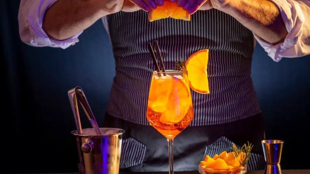 Bartender sirviendo una bebida con trozos de naranja.