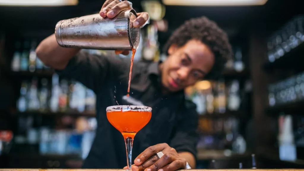 Bartender sirviendo una bebida de color anaranjado.