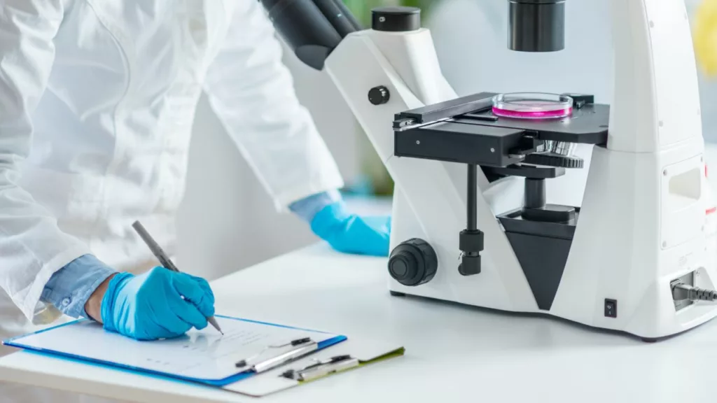Científico anotando el comportamiento de las muestras, vistas desde un microscopio.
