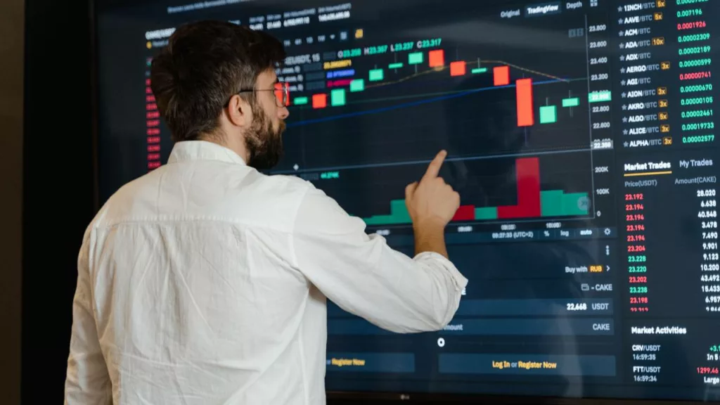 Agente de bolsa de valores mirando una pantalla con datos financieros del mercado.