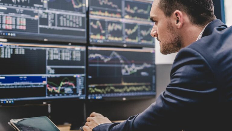 Hombre trabajando como corredor o agente de bolsa de valores en su oficina, con varias pantallas de trading.