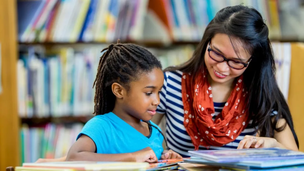 Bibliotecario ayudando a una niña a leer un libro.