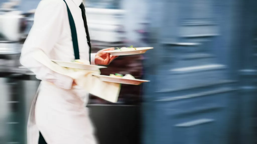 Camarero con 3 platos para servir en la mesa de un restaurante.