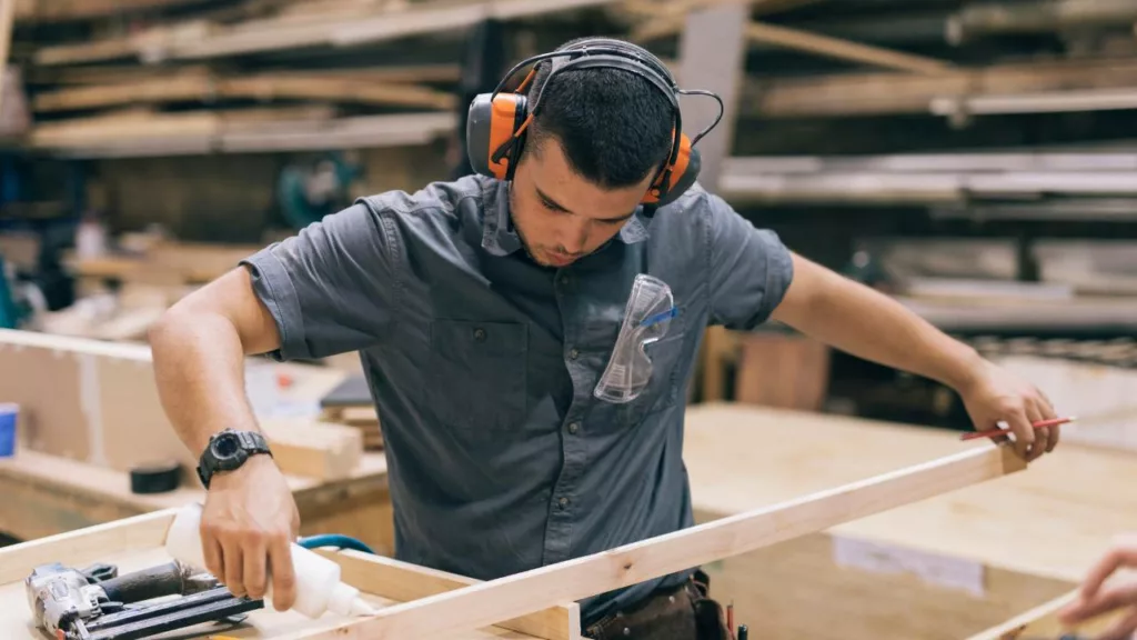 Joven carpintero sosteniendo una madera y colocando pegamento de construcción.