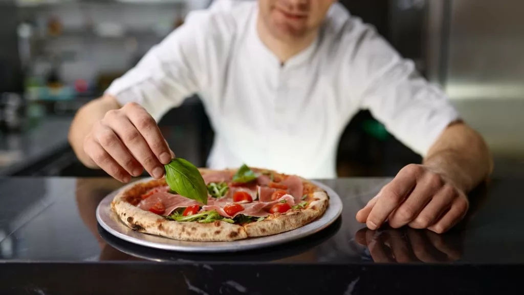 Chef colocando ingredientes a la pizza que ha cocinado.