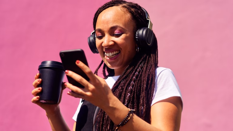 Community Manager disfrutando de contenido digital con auriculares y smartphone, mostrando un estilo moderno y relajado con fondo rosa vibrante.